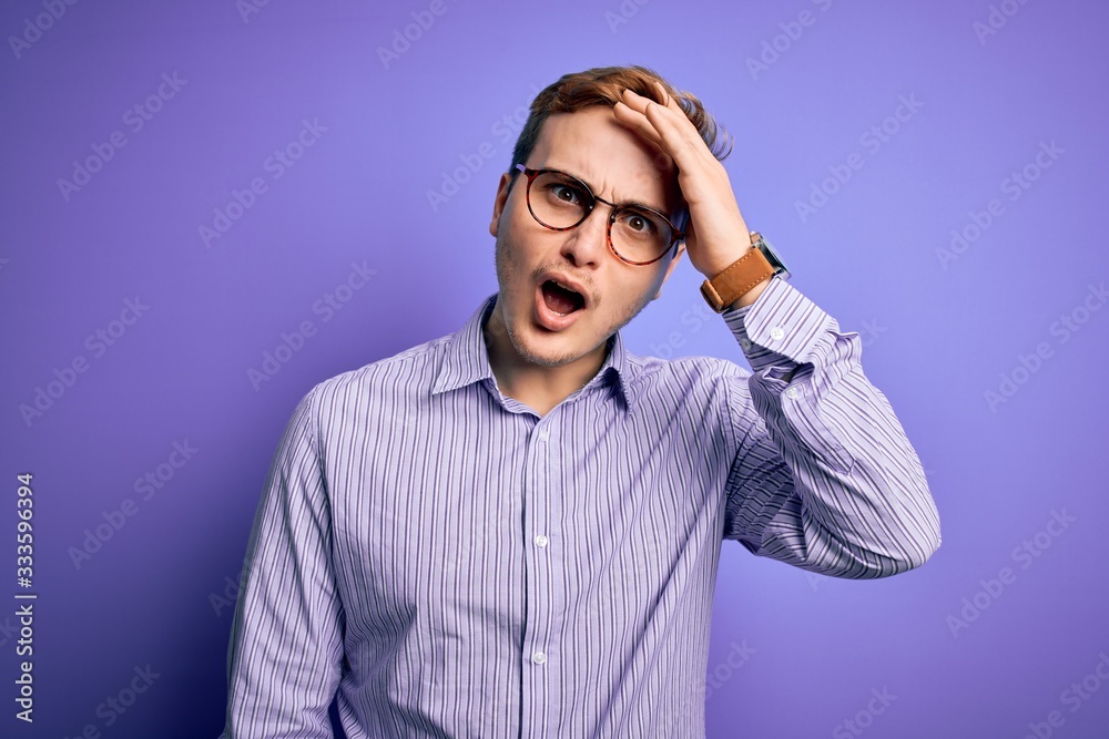 Young handsome redhead man wearing casual shirt and glasses over purple background surprised with hand on head for mistake, remember error. Forgot, bad memory concept. Young handsome redhead man wearing casual shirt and glasses over purple background surprised with hand on head for mistake, remember error. Forgot, bad memory concept.