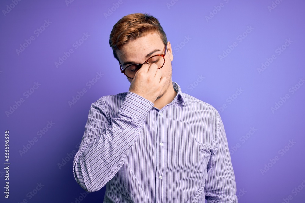 Young handsome redhead man wearing casual shirt and glasses over purple background tired rubbing nose and eyes feeling fatigue and headache. Stress and frustration concept.