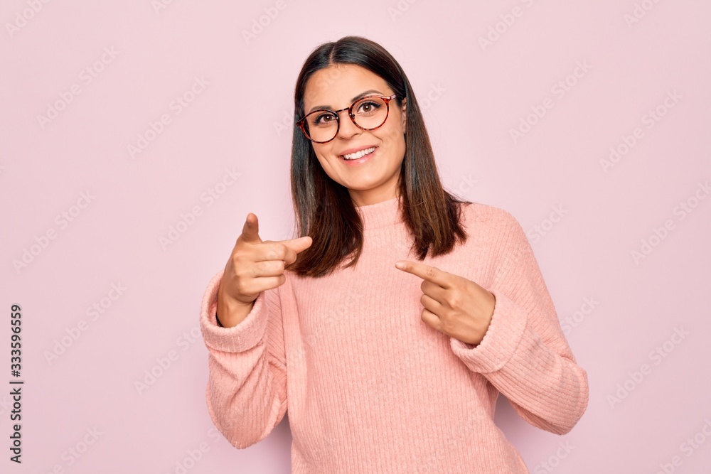 Young beautiful brunette woman wearing casual sweater and glasses over pink background pointing fingers to camera with happy and funny face. Good energy and vibes. Young beautiful brunette woman wearing casual sweater and glasses over pink background pointing fingers to camera with happy and funny face. Good energy and vibes.