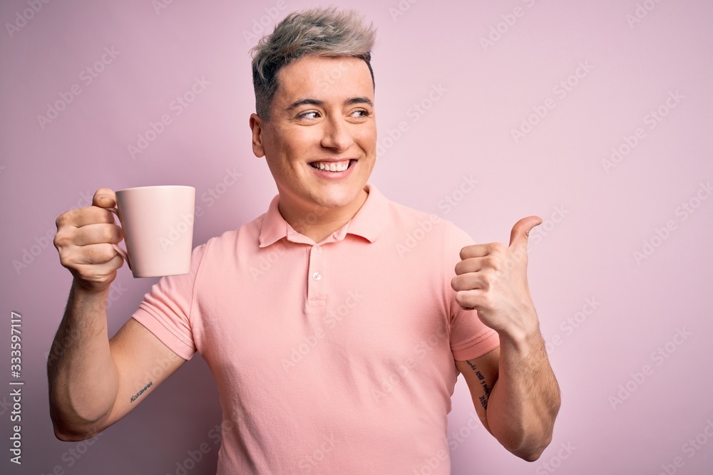 Young modern handsome man drinking a cup of hot coffee over isolated pink background pointing and showing with thumb up to the side with happy face smiling Young modern handsome man drinking a cup of hot coffee over isolated pink background pointing and showing with thumb up to the side with happy face smiling