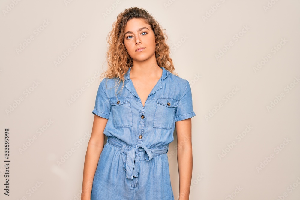Young beautiful woman with blue eyes wearing casual denim dress over white background Relaxed with serious expression on face. Simple and natural looking at the camera.