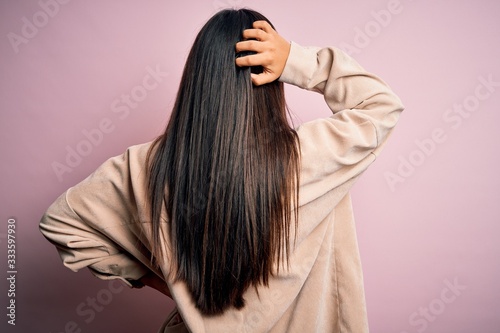 Young beautiful asian woman wearing casual shirt standing over pink background Backwards thinking about doubt with hand on head