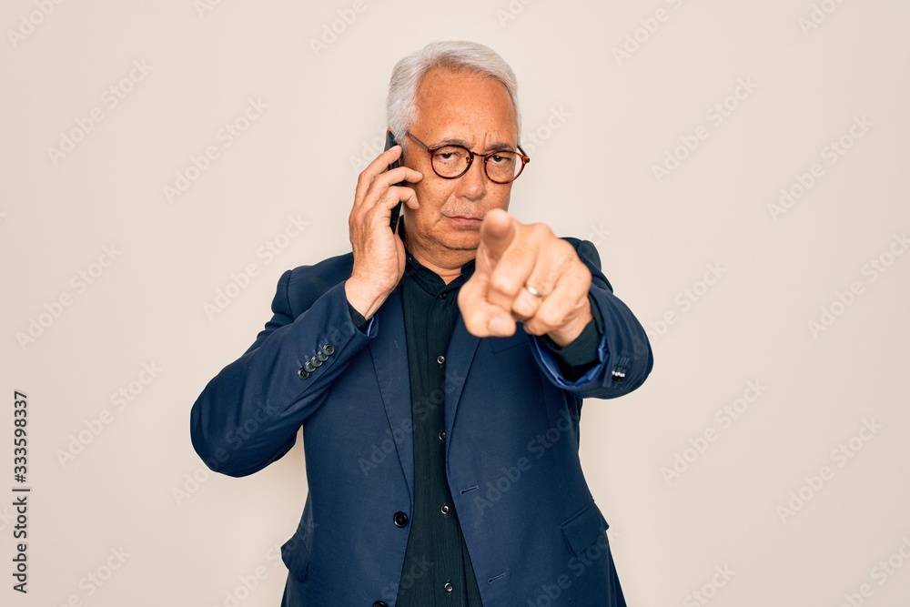 Middle age senior grey-haired business man wearing glasses talking on smartphone pointing with finger to the camera and to you, hand sign, positive and confident gesture from the front Middle age senior grey-haired business man wearing glasses talking on smartphone pointing with finger to the camera and to you, hand sign, positive and confident gesture from the front