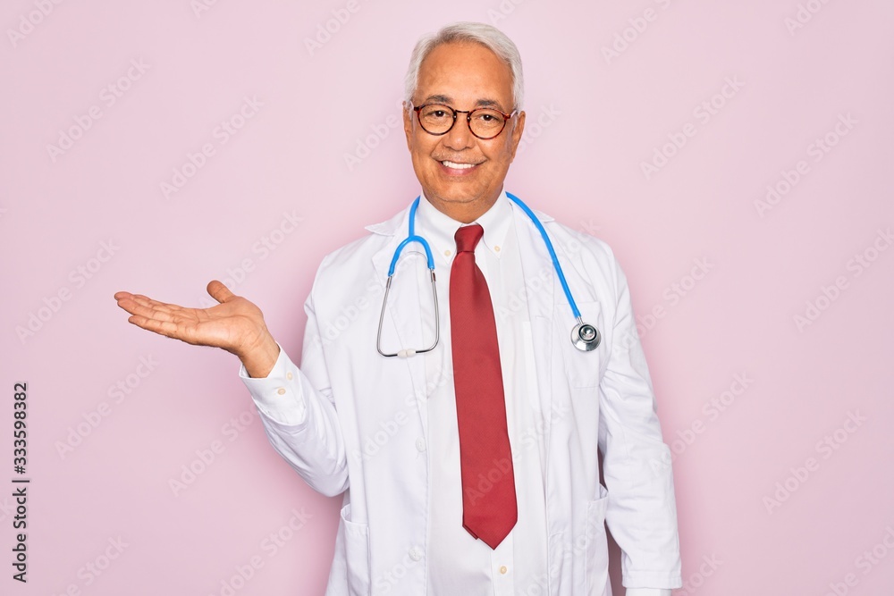 Middle age senior grey-haired doctor man wearing stethoscope and professional medical coat smiling cheerful presenting and pointing with palm of hand looking at the camera. Middle age senior grey-haired doctor man wearing stethoscope and professional medical coat smiling cheerful presenting and pointing with palm of hand looking at the camera.