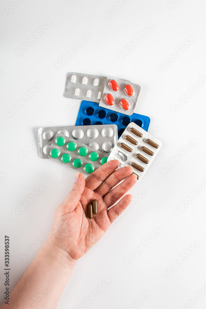 Capsules in a female hand on a background of colorful pills and capsules in blister packs on a white background. Coronavirus. Pharmaceutical industry. Antibiotics Capsules in a female hand on a background of colorful pills and capsules in blister packs on a white background. Coronavirus. Pharmaceutical industry. Antibiotics
