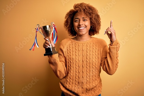 Canvas Print Young African American afro woman with curly hair holding winner champion trophy