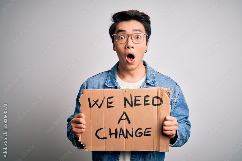 Young handsome chinese activist man protesting asking for change holding poster scared in shock with a surprise face, afraid and excited with fear expression