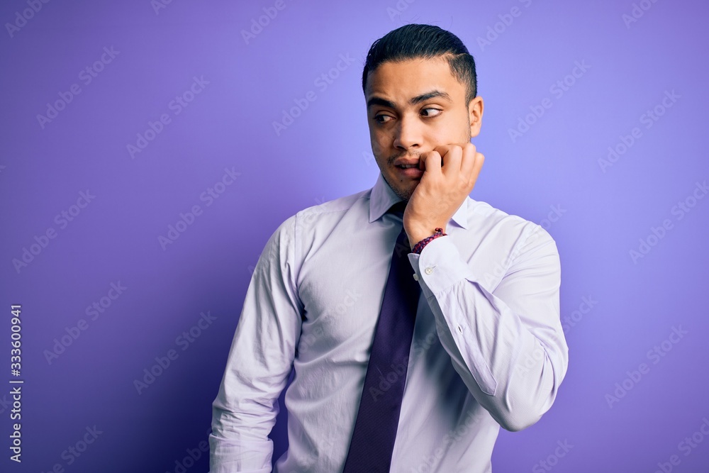 Young brazilian businessman wearing elegant tie standing over isolated purple background looking stressed and nervous with hands on mouth biting nails. Anxiety problem. Young brazilian businessman wearing elegant tie standing over isolated purple background looking stressed and nervous with hands on mouth biting nails. Anxiety problem.
