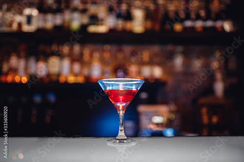 Barman is preparing red alcoholic cocktail with blue smoke in martini glass, decorated with orange