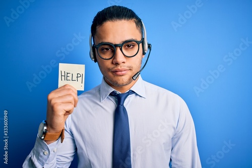 Young brazilian call center agent man overworked holding reminder paper with help message with a confident expression on smart face thinking serious