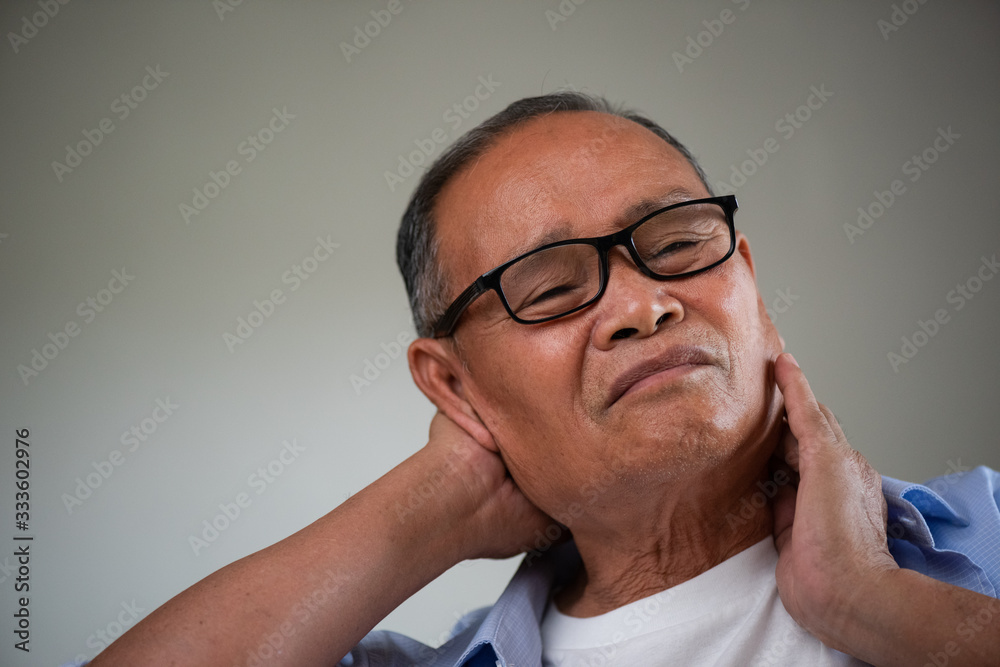 Asian old man sitting on sofa and having neck pain, backache at home. Senior healthcare concept.