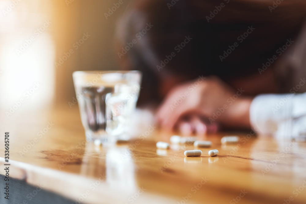 Closeup image of a sick woman sleep on table with white pills and a glass of water Closeup image of a sick woman sleep on table with white pills and a glass of water