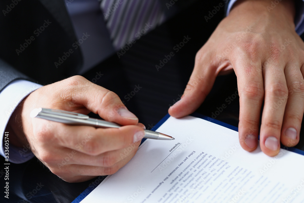 Male arm in suit and tie fill form clipped to pad with silver pen closeup. Sign gesture read pact sale agent bank job make note loan credit mortgage investment finance chief legal law concept Male arm in suit and tie fill form clipped to pad with silver pen closeup. Sign gesture read pact sale agent bank job make note loan credit mortgage investment finance chief legal law concept