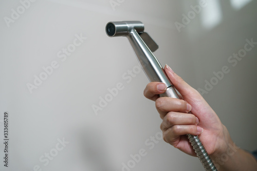 Woman hand using Chromium bidet shower sitting on toilet. photo