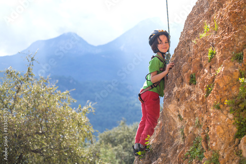 A boy in helmet climbs a rock on a background of mountains.