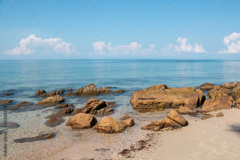 Brown rocks get affected by sea wave on a tropical beach with blue sky
