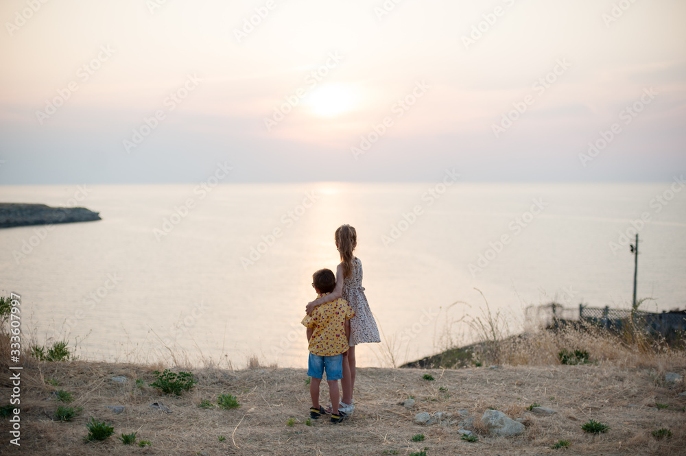 care dream and love and hope concept of two little children boy and girl hugging on sea shore looking at warm summer sunset during leisure holiday with copy space