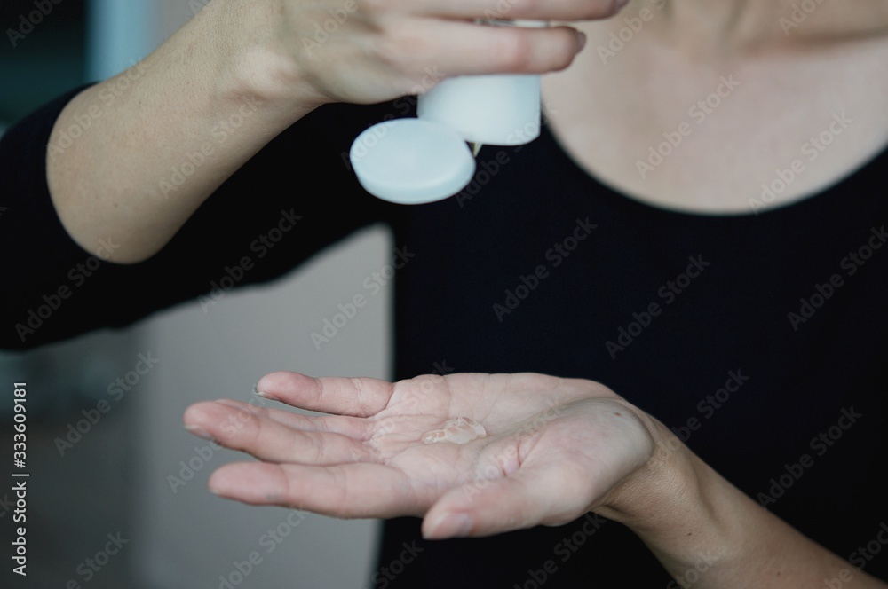 Fototapeta premium A woman stay at home with a medical protective, a means of protection against the virus, uses alcohol gel 70% to disinfect hands. Epidemia Coronavirus. Covid-19