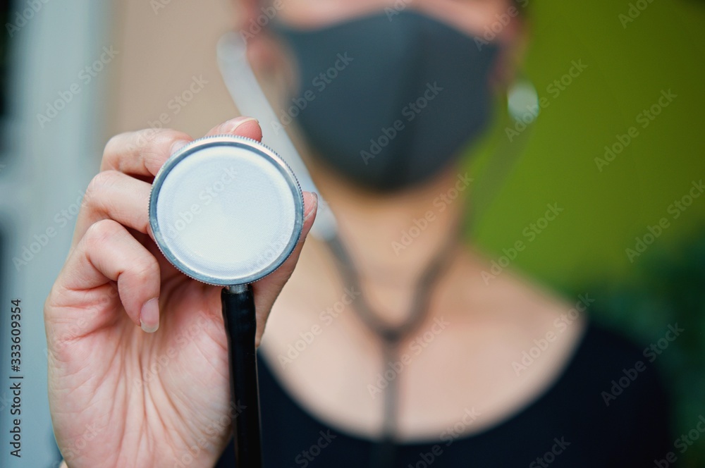 Fototapeta premium Asian woman wearing facial mask for protection from air pollution or virus epidemic and holding Stethoscope in her hand, she worried about Covid-19 situations.