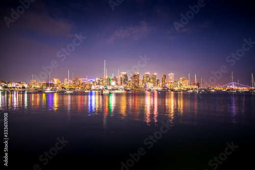 The lights of San Diego's skyline reflect off the waters of the Pacific Ocean, with sailboats in the foreground. © Chris