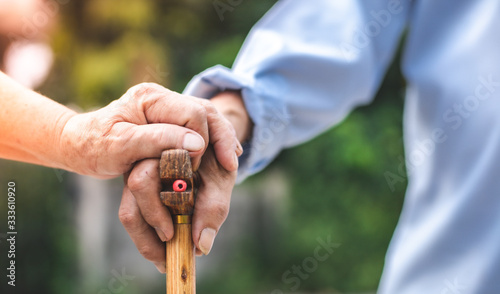 Close up of elderly hands in wrinkles holding walking stick.elderly old man with walking stick stand on footpath sidewalk crossing. © anon
