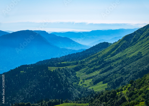 View over the Green Valley, surrounded by high mountains on a clear summer day. Layers of mountains in the haze during sunset.