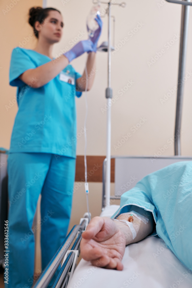 Nurse hanging IV bag on stand while giving IV fluids to ill patient in  hospital Stock Photo
