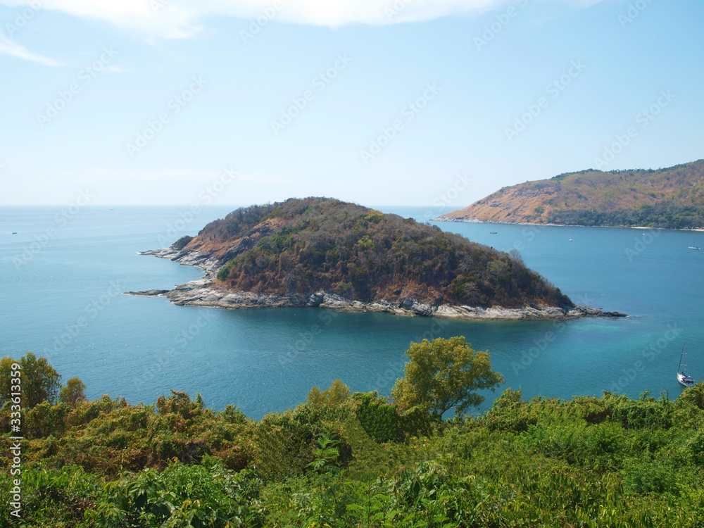 Island near the green coast line of the azure sea. View from the land shore. Panoramic colorful view of blue water, sky, cloud and islands. Seascape of wild nature.