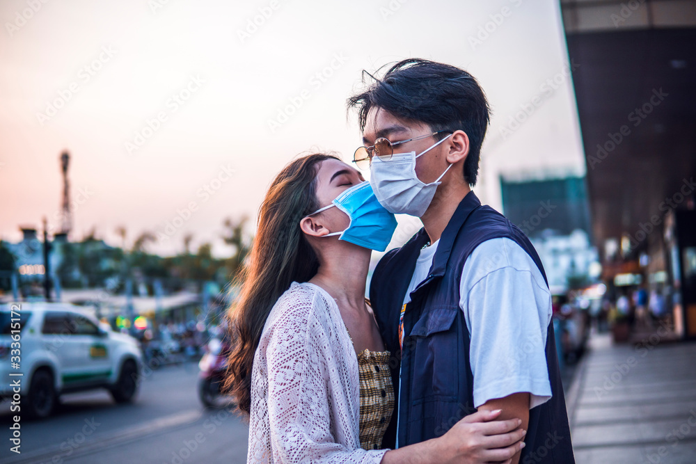 Lover man and girl kiss in protective masks respirator on city night background, people affected epidemic virus, spread airborne droplets.