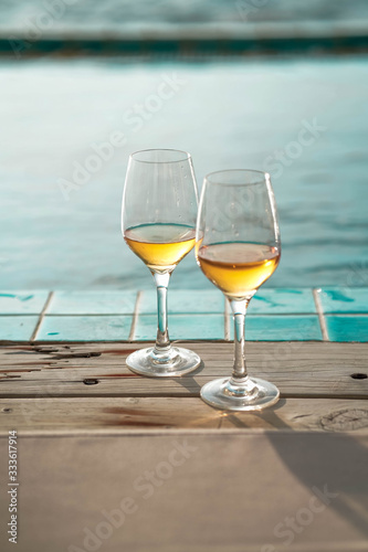 Two glasses of wine on the edge of infinity swimming pool with panoramic views of the sea at sunset. Drink, celebrate, vacation and summer concept.