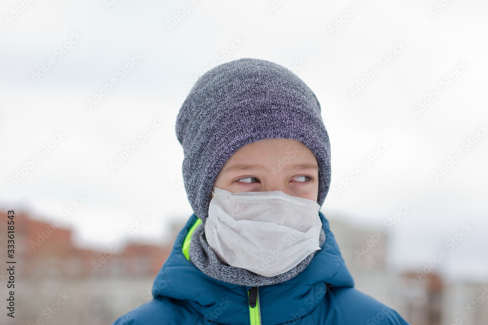 The danger of coronavirus. A boy on a walk walks in a medical mask on his face The danger of coronavirus. A boy on a walk walks in a medical mask on his face