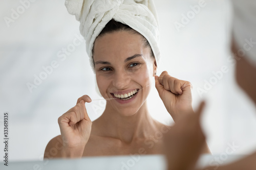 Pretty smiling woman with bath towel on head use floss cleans teeth remove food between tooth preventing disease such as gingivitis, caries. Personal dental care, oral hygiene, morning routine concept