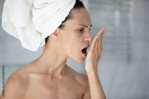 Woman with towel on head put palm in front face opens mouth check breath close up image. Suffers from unpleasant odor due to oral infections, poor dental hygiene, health problems, halitosis concept photo