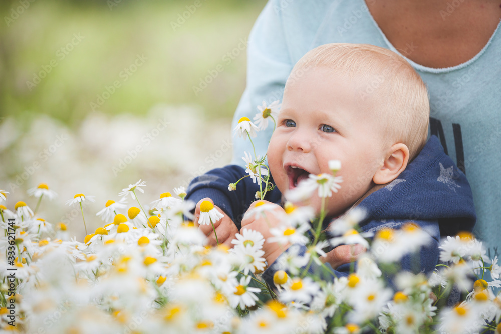 Cute, charming smiling baby in a blue jacket in the arms of a young woman. A child learns nature, collects wild, beautiful summer flowers with his mother. Summer concept Cute, charming smiling baby in a blue jacket in the arms of a young woman. A child learns nature, collects wild, beautiful summer flowers with his mother. Summer concept