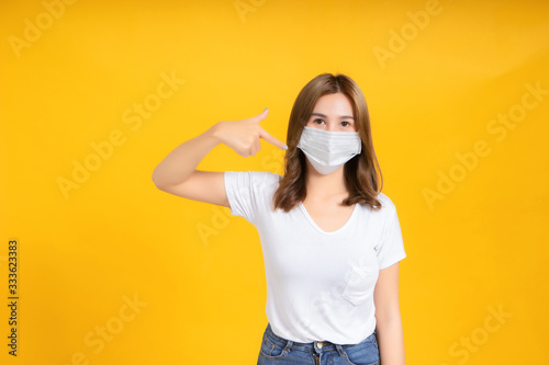 Asian women pointing finger and wear correct masks to protect against germs from coronavirus, covid-19, pm2.5 dust and prevent infections on a yellow background, healthy concept.