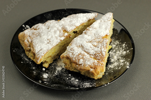 Delicious apple pie, charlotte is sprinkled with powdered sugar on a black plate on a dark background. The view top