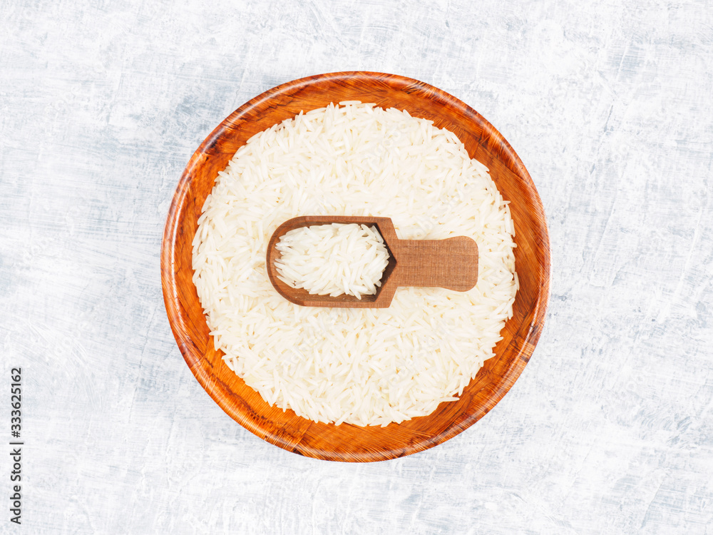 Indian long grain Basmati rice in brown wooden bowl and in scoop on white concrete background Indian long grain Basmati rice in brown wooden bowl and in scoop on white concrete background