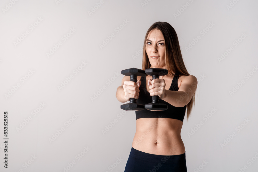 Strong muscular girl working out with dumbbells. Photo of attractive sporty girl isolated on white background. Strength and motivation
