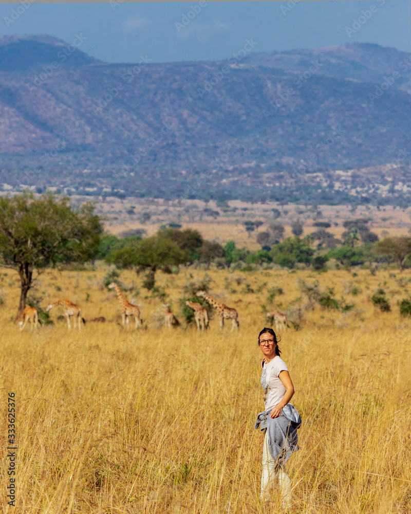 Young woman enjoying a walking safari in Uganda, Africa, with giraffes in the background.