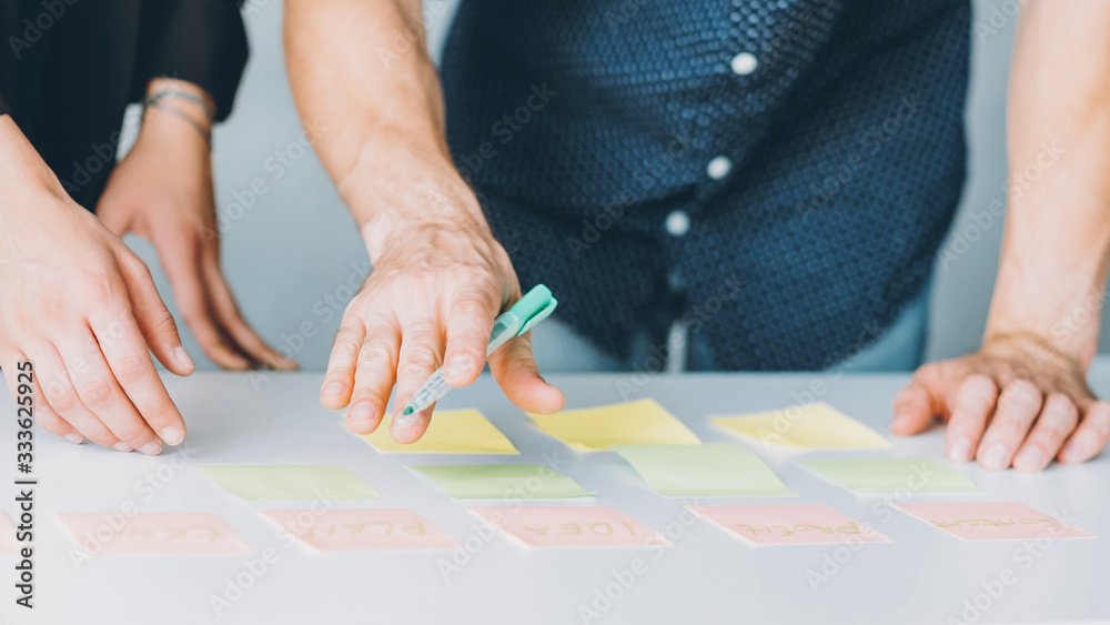 Project management. Teamwork brainstorming. Colleagues writing ideas on sticky notes. Project management. Teamwork brainstorming. Colleagues writing ideas on sticky notes.