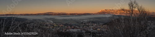 Panorama of the city of Postojna in Slovenia in early winter morning with sun just rising up and lighting mountain ridge of Nanos in the background. Beautiful early panorama of a small city.