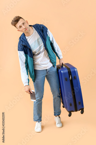 Tired male tourist with luggage on color background