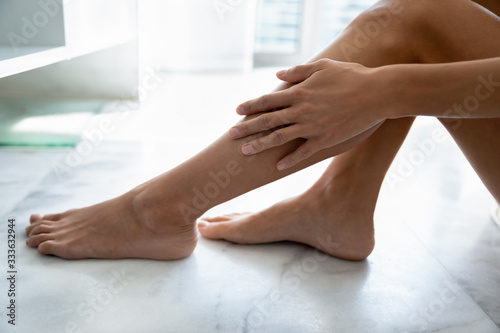 Close up female sit on tiled floor in modern bath room touches legs with hand enjoy soft smooth silky skin after epilation home shugaring procedure, cream for perfect skin, skincare, bodycare concept © fizkes