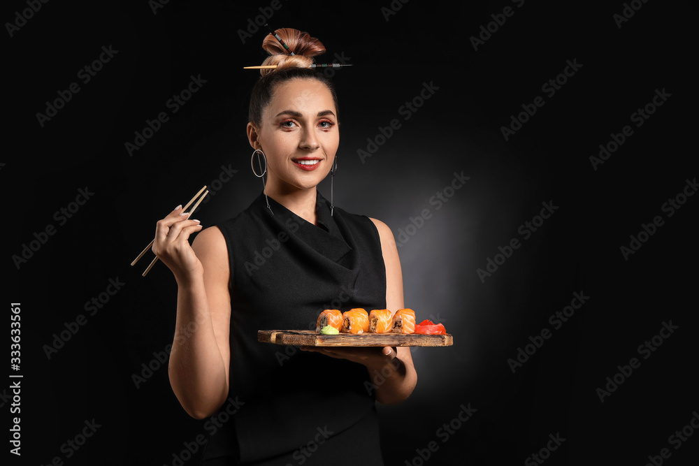 Fototapeta premium Smiling woman holding a wooden board with fresh salmon sushi rolls, wasabi, and pickled ginger