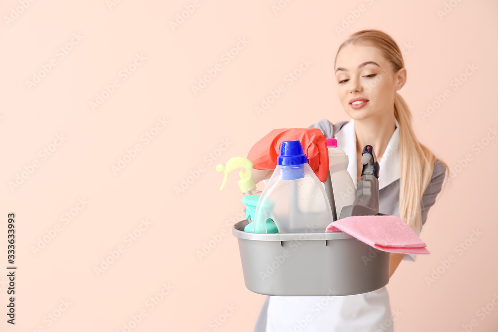 Beautiful young chambermaid with cleaning supplies on color background Beautiful young chambermaid with cleaning supplies on color background