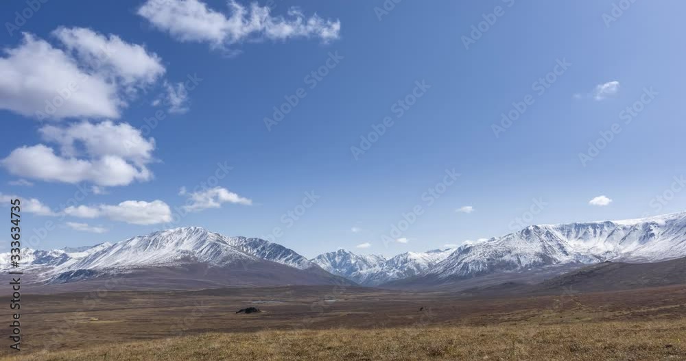 Timelapse of sun movement on crystal clear sky with clouds over snow mountain top. Yellow grass at autumn high altitude meadow. Wild endless nature. Timelapse of sun movement on crystal clear sky with clouds over snow mountain top. Yellow grass at autumn high altitude meadow. Wild endless nature.