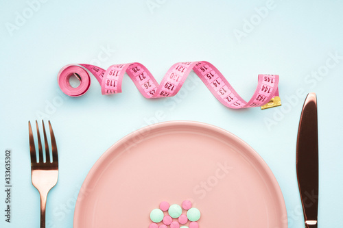 Plate with weight loss pills, cutlery and measuring tape on color background
