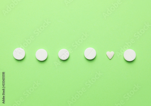 Heart-shaped pill among round ones on color background