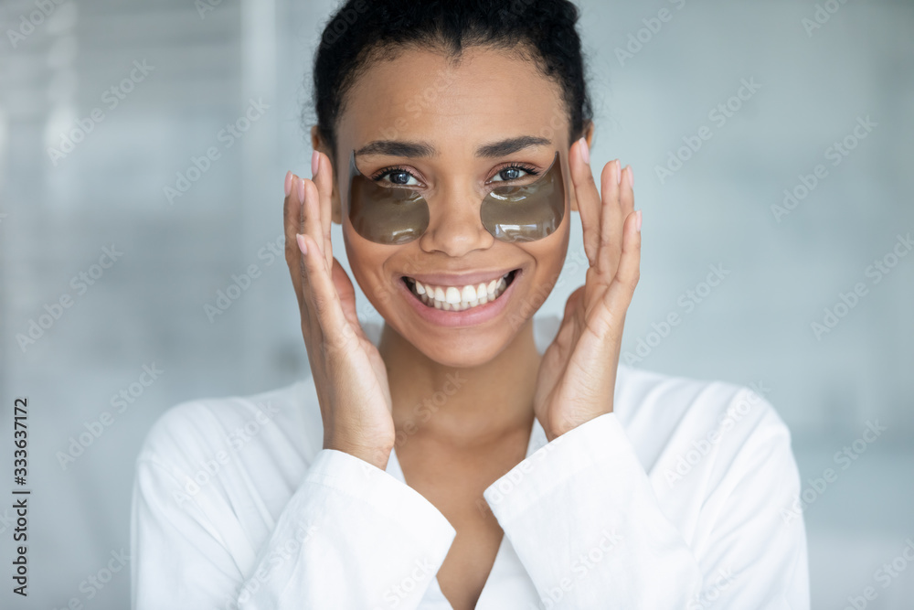 Happy beautiful 35s african young woman apply under eye hydrogel patches. Helpful trendy beauty treatment for reduce puffiness, remove dark circles and getting rid of fine wrinkles, skin care concept Happy beautiful 35s african young woman apply under eye hydrogel patches. Helpful trendy beauty treatment for reduce puffiness, remove dark circles and getting rid of fine wrinkles, skin care concept