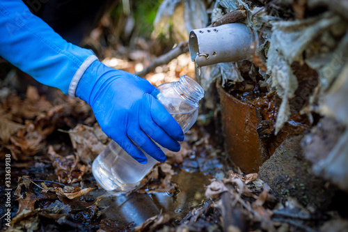 Ecologist taking water samples from a natural source in protective gloves